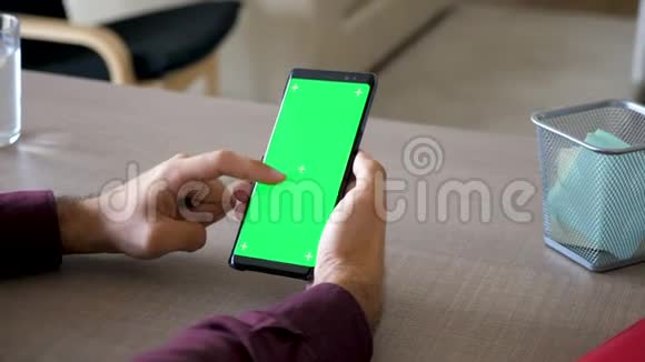 男人的手在智能手机上滚动绿色屏幕色度模拟在他的办公桌上视频的预览图
