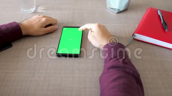 带有绿色屏幕颜色的智能手机在桌子上模拟男性手在上面工作视频的预览图