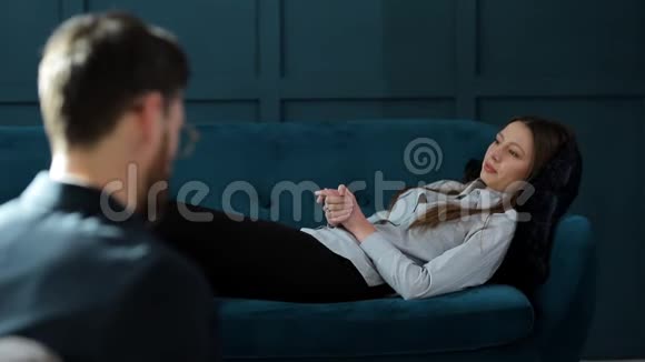 年轻女性在豪华的蓝色心理治疗中在舒适的沙发上看男心理学家视频的预览图