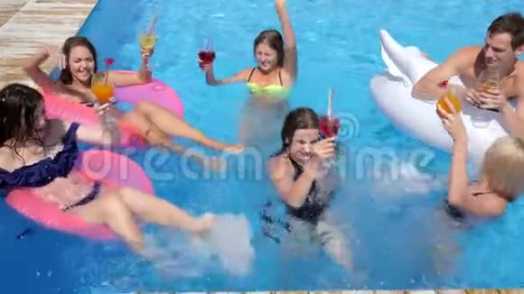 泳池派对豪华的生活朋友带着彩色鸡尾酒在充气环上游泳进入游泳池视频的预览图