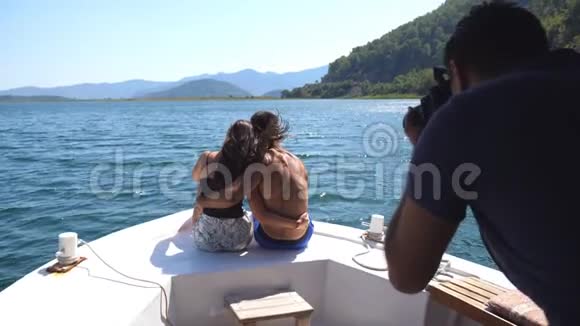 年轻的一对坐在船头向无法辨认的摄影师摆姿势快乐的一对相爱的人在一起视频的预览图