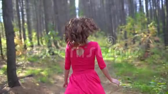 美丽的女孩穿着红色的裙子在森林里长着健康的长发肖像秋天快乐的女人慢动作微笑视频的预览图
