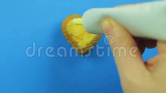 女性的手在蓝色背景上涂上心形饼干黄色的糖霜来自一张滑稽的脸视频的预览图