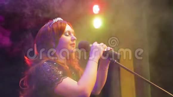 年轻的红发女歌手在台上用一阵烟在麦克风前唱歌视频的预览图