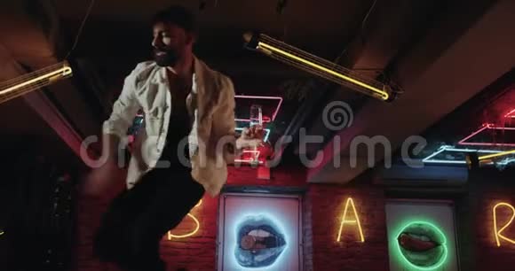 有魅力的男人留着胡子跳舞在酒吧的桌子上放着一杯香槟在黑暗的咖啡馆里迪斯科灯视频的预览图