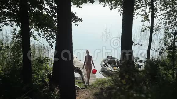 一个女人带着水桶走在湖边的码头上视频的预览图