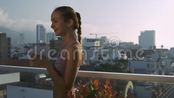 女孩在屋顶露台上喝咖啡靠城市视频的预览图