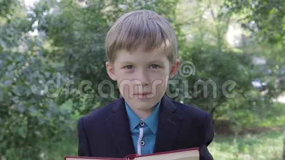 一个手里拿着书的男孩在玩他的脸这个男孩从书后面看起来很有趣穿夹克的男孩视频的预览图