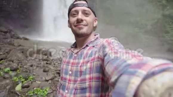 自私的男人男子在瀑布附近拍照并展示拇指视频的预览图