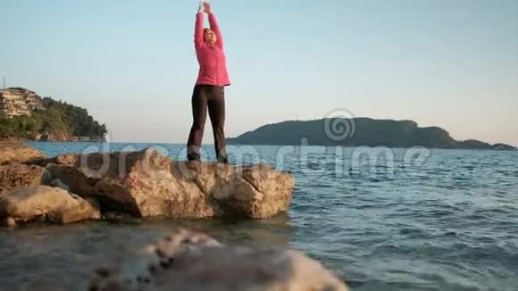 日落时一个女人站在岩石上湖边沉思视频的预览图