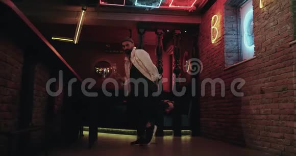 在酒吧里穿着白色夹克的年轻人在闪烁着彩色灯光的快乐背景下跳舞视频的预览图