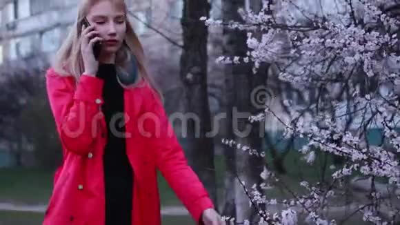 小女孩走过春暖花开的花园在智能手机上交谈视频的预览图