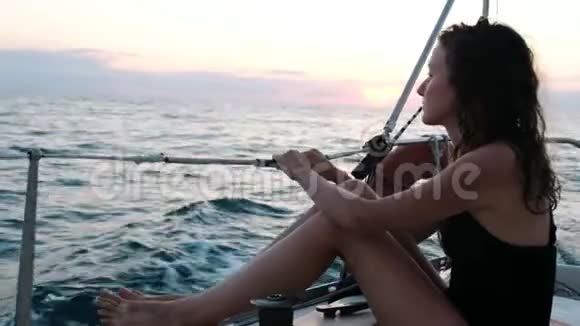 身穿泳装的女人坐在游艇的船尾日落时欣赏海景视频的预览图