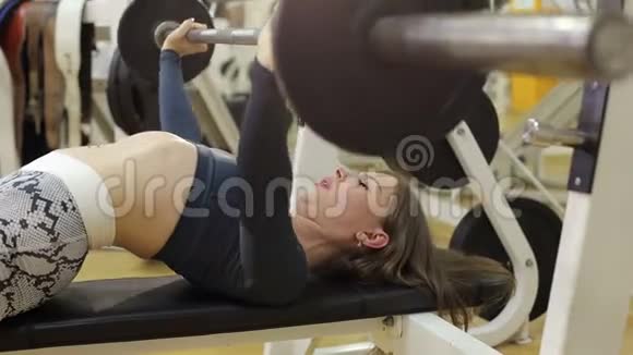 运动的女孩在健身房里用一个仰卧位的酒吧做运动视频的预览图