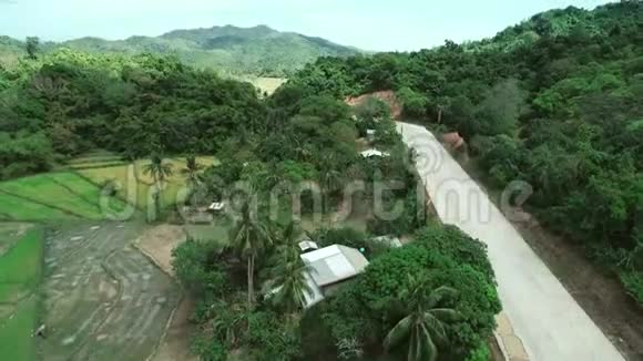 透过茂密的绿色植物和茂密的热带雨林山地景观的乡村道路鸟瞰视频的预览图