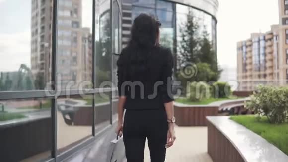 漂亮的商务女性穿着严格的西装带着文件夹靠近商务中心背面视图视频的预览图