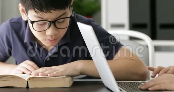 亚洲十几岁男孩提防眼镜在家里用笔记本电脑可爱的男孩认真地做作业视频的预览图