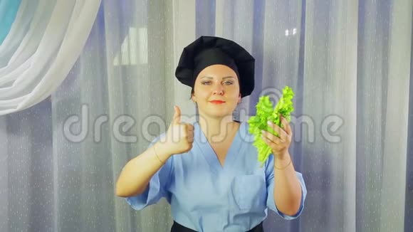 女厨师穿着围裙微笑手拿绿色沙拉用手展示课堂视频的预览图