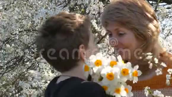子给妈妈送花妈妈和儿子在一棵开花树的背景下母亲节视频的预览图
