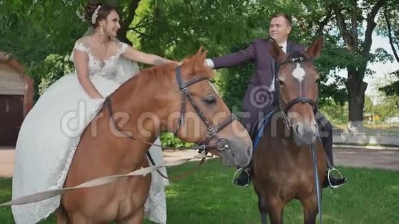 婚礼当天新郎新娘牵着手坐在美丽的绿色公园里骑着华丽的马视频的预览图