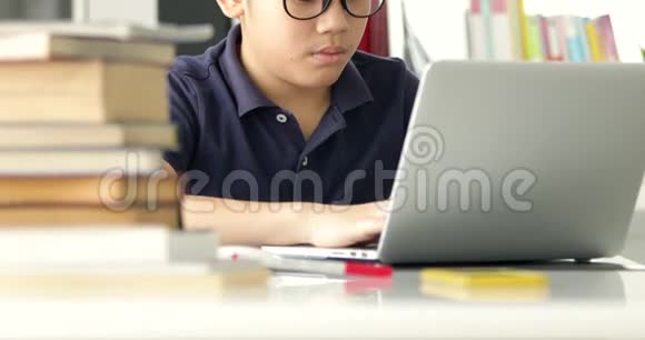 亚洲十几岁男孩提防眼镜在家里用笔记本电脑可爱的男孩认真地做作业视频的预览图