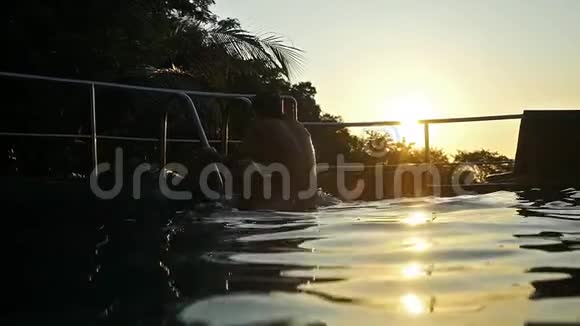 年轻人在夕阳下的游泳池里跳着水在夕阳下翻滚水在美丽的波克中飞溅视频的预览图