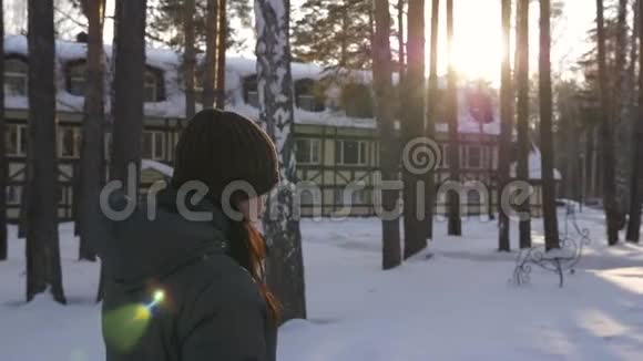 年轻女子走在冬天的村舍里在桦树和松树之间太阳耀斑视频的预览图