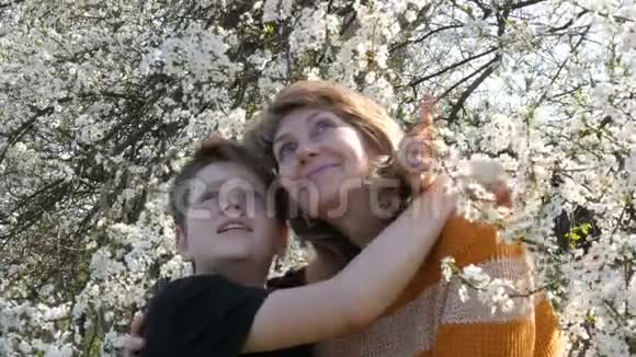 一位成年中年母亲和她十几岁的儿子在一棵盛开的树上仰望天空的肖像视频的预览图