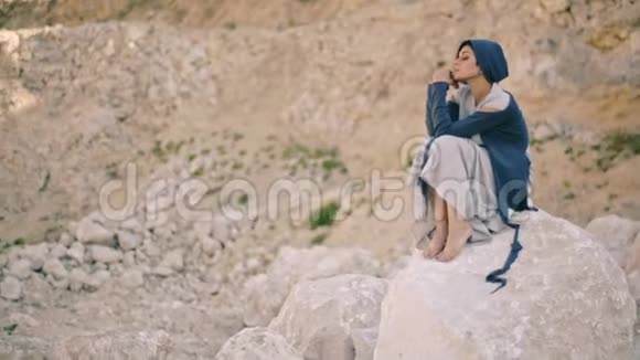 悲伤的年轻女子坐在山间的岩石上视频的预览图