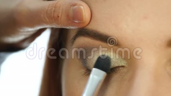特写化妆师的手用画笔将眼影涂在女人眼睛上慢动作视频的预览图