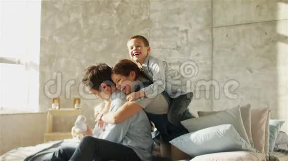 一位年轻的父亲和三个孩子抱着坐在床上快乐的父亲父亲节视频的预览图