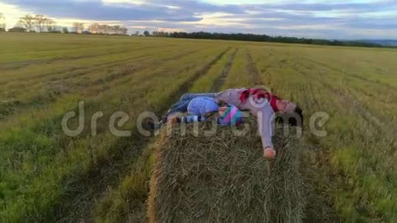 母亲和女儿躺在夕阳下乡村田野上的草垛上视频的预览图