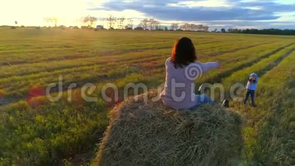 母亲坐在稻草堆上在夕阳下的乡村田野上牵着女儿的手视频的预览图