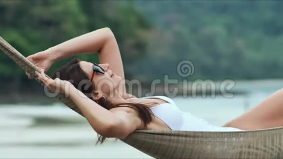 戴太阳镜的年轻美女在热带海滩的吊床上放松视频的预览图