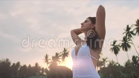 穿着白色泳衣留着长发在海滩日落时摆姿势的性感女孩视频的预览图