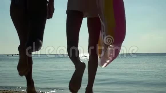 年轻快乐的夫妇牵着手拿着床垫跑到海里在床垫上在海里游泳慢动作视频的预览图