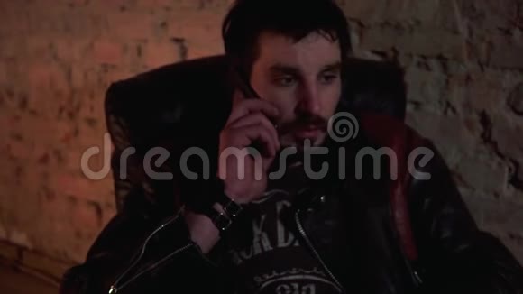 一个穿着皮夹克的男人坐在皮扶手椅上打电话视频的预览图