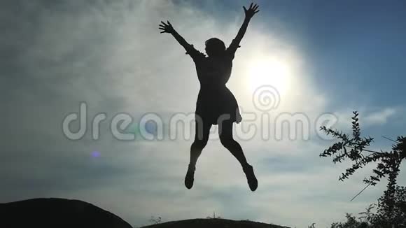 年轻快乐的女人跳在岩石前的太阳剪影与悬崖慢动作1920x1080视频的预览图