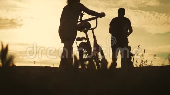 比基尼家庭剪影父母带着两个孩子骑自行车在日落友好家庭观念视频的预览图