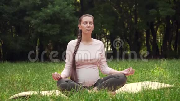 一位孕妇坐在地毯上坐在莲花的位置在公园里练习瑜伽视频的预览图