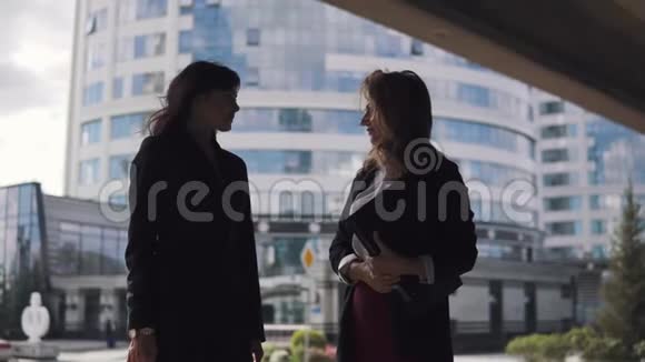 商业中心背景上的商人剪影两个商务女性面对面交谈颤抖着视频的预览图
