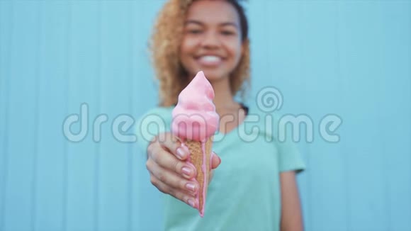 年轻的非洲女孩在蓝墙背景下吃粉色融化冰淇淋视频的预览图
