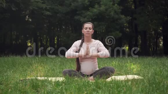 一位孕妇坐在地毯上坐在莲花的位置在公园里练习瑜伽视频的预览图