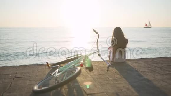 年轻漂亮的长发女人在日落或日出时在海上玩得很开心有自行车的女人后面的游艇视频的预览图
