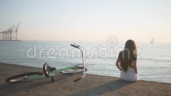 年轻漂亮的长发女人在日落或日出时在海上玩得很开心有自行车的女人后面的游艇视频的预览图
