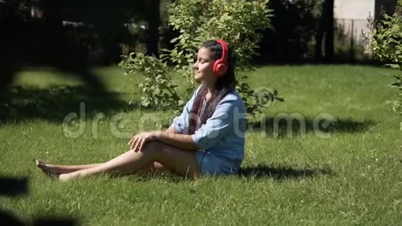 留着长发的小女孩坐在公园的草地上听着耳机里的音乐视频的预览图