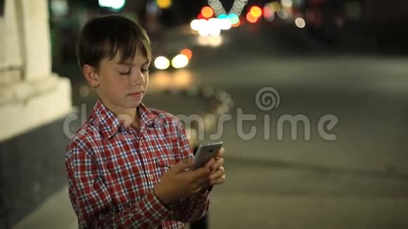 男孩手里拿着智能手机背景是夜城的灯光视频的预览图