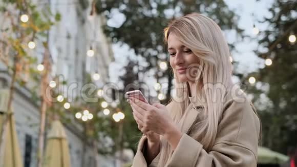 秋装女人在户外智能手机上写信息的肖像使用数码小工具的女孩卷轴视频的预览图