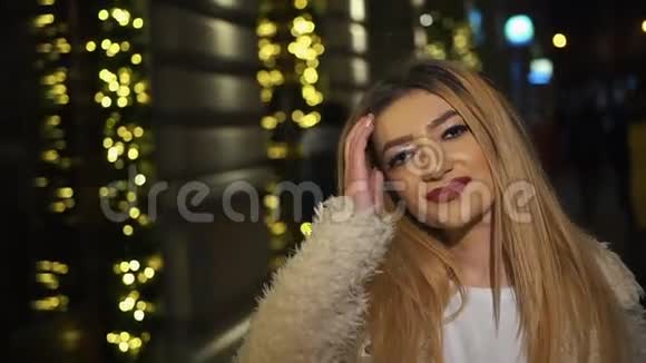 美丽的变性女人站在城市广场的圣诞装饰和修复她的金色长发视频的预览图