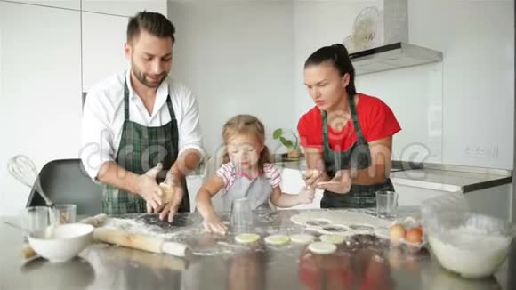 可爱的小女孩和她美丽的父母正在做饭他们在一起玩得很开心在家里的厨房里微笑视频的预览图